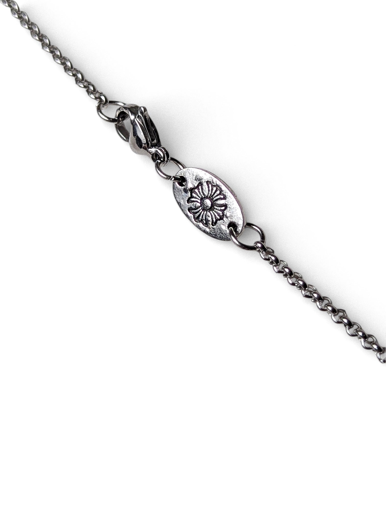 Detailed view of floral engraved oval tag and lobster clasp on silver layered necklace